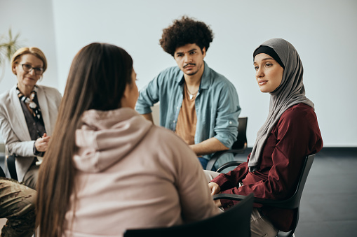 Young Muslim woman talking to group therapy members during their meeting at mental health center.
