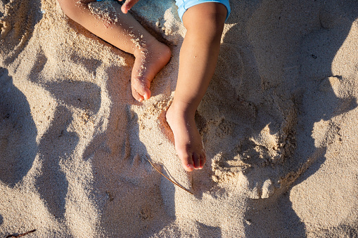 View from above of a baby's feet playing on the beach.