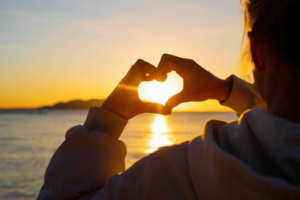 istock Heart shape with female hands over sunset sky background 1386401146