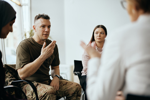 Soldado adulto medio compartiendo su historia con los asistentes a la terapia de grupo en el centro de salud mental. photo