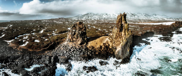 Londrangar Cliffs - Lóndrangar Rock Pinnacles at the icelandic coast of Snaefellsnes in Vesturland (West Central Iceland) towards North Atlantic Ocean. The Lóndrangar are uniquely-formed remnants of ancient basalt volcanic dikes sticking out from the sea. XXXL Stiched Mavic3 Drone Panorama Shot in late Winter Season. Lóndrangar, Snæfellsnes Peninsula, West-Central Iceland, Nordic Countries, Europe.