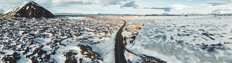 Icelandic Country Road along frozen Lake Mývatn in Winter. Route 1 to the horizon on a sunny cold winter day. Aerial Drone Point of View Stiched Mavic 3 Panorama. Mývatn - myvatn Lake, Northern Iceland, Iceland, Nordic Countries, Northern Europe.