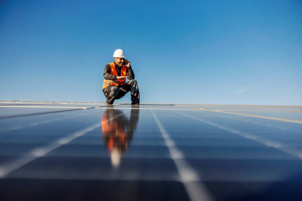 istock A handyman talking on the phone charged by solar power while crouching surrounded solar panels. 1386418118