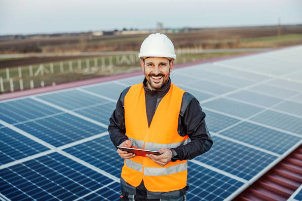 a handyman holding tablet for checking on solar panels and smiling at the camera. - environmental portrait imagens e fotografias de stock
