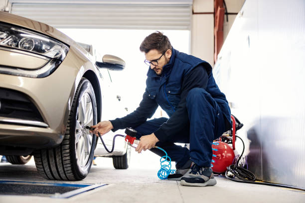 A focused auto mechanic inflates the tire at workshop. A mechanic crouching next to a car and inflates the tire at workshop. inflating stock pictures, royalty-free photos & images