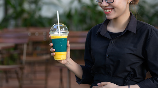 Smile asian waitress holding a mango smoothie in a plastic takeout cup