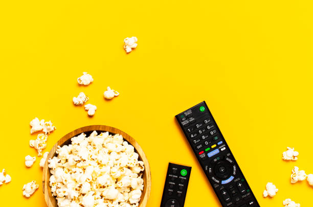 istock Black TV, audio remote control and popcorn on bright yellow background flat lay top view copy space. Minimalistic background with a remote control, watching a movie, series, set-top boxes, audio system 1386436327