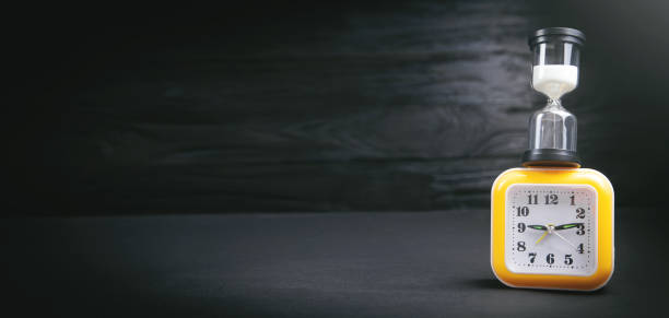istock Yellow clock and hourglass on the dark background. 1386436456