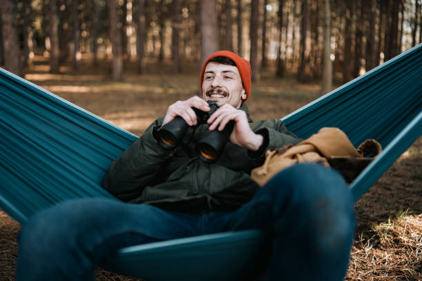 istock Young adult man sitting in hammock and looking with binoculars 1386436710