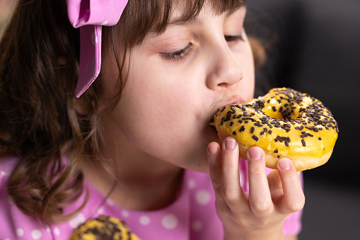 Portrait of young hungry girl eating donut. Female mouth bites a loaf. Close-up woman eating donut , delicious, sweet, sweet tooth at home background