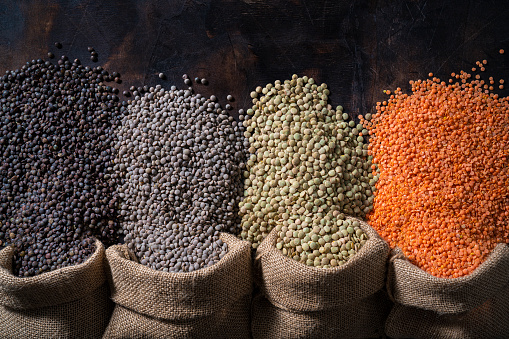 Assorted dried lentils legumes in burlap sacks bags as red lentils, brown and green lentils dupuy on rustic dark wooden background leaving copy space