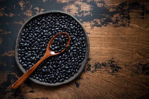 black beans frijoles getrocknete hülsenfrüchte in einem teller mit löffel auf rustikalem dunklem holzhintergrund und lassen kopierraum - frijoles stock-fotos und bilder