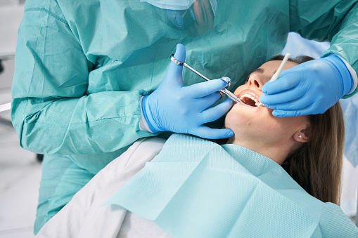 Female patient lying on dental chair while doctor in sterile gloves doing local anesthesia injection before dental procedure
