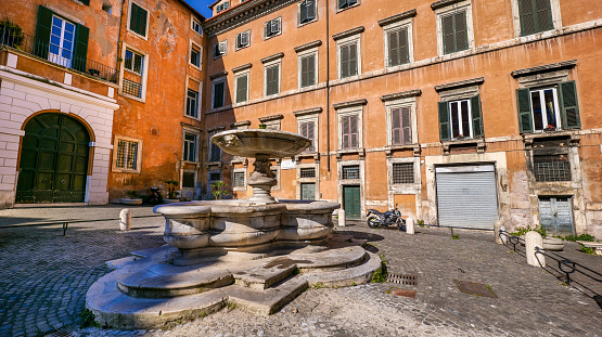 A glimpse of the ancient Piazza Delle Cinque Scole in the heart of the Jewish Quarter of Rome (Roman Ghetto), in the historic core of the Eternal City. In the center, the Fontana delle Cinque Scole or Fontana del Pianto, a fountain built between 1591 and 1593 by the architects Giacomo della Porta and Pietro Gucci. The iconic Jewish Quarter of Rome, the oldest ghetto in Europe, is famous for the presence of hidden alleys and small squares, where it is easy to find small restaurants of Italian and Jewish cuisine, and remarkable Roman archaeological remains. The ghetto of Rome is located in one of the oldest districts of the Eternal City, between the Campidoglio (Roman Capitol) and the Tiber river. In 1980 the historic center of Rome was declared a World Heritage Site by Unesco. Super wide angle image in 16:9 and high definition format.