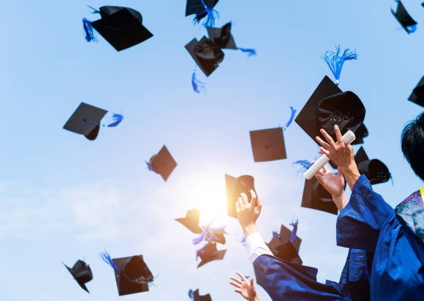 las manos de los estudiantes que se gradúan lanzando gorras de graduación al aire - birrete fotografías e imágenes de stock