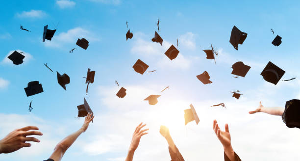 las manos de los estudiantes que se gradúan lanzando gorras de graduación al aire - graduaciones fotografías e imágenes de stock