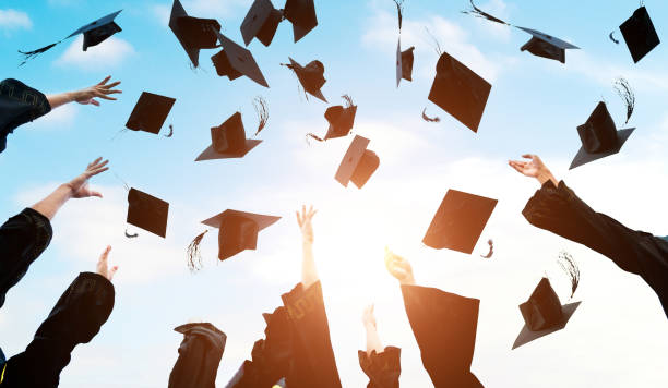 istock Graduating students hands throwing graduation caps in the air 1386452730