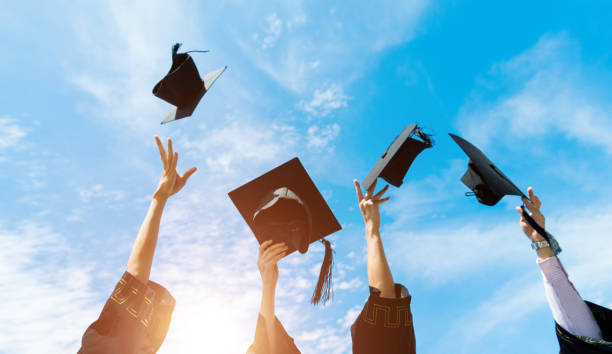 quatre diplômés lançant des chapeaux de fin d’études en l’air - toque de diplômé photos et images de collection