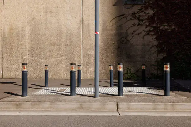 Black metal bollards surround a metal door in a footpath.