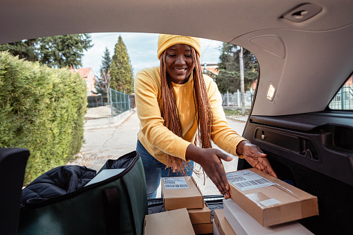 Female delivery person Black ethnicity loading and organizing packages for delivery in her delivery van/car trunk