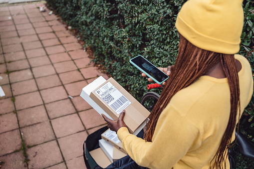 Unrecognizable female delivery person Black ethnicity scanning the bar code on package with mobile phone