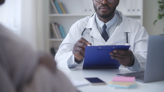African American gynecologist writing down test results during pregnant woman health check-up