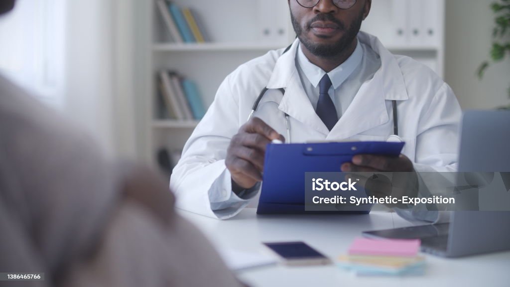 African American gynecologist writing down test results during pregnant woman health check-up Doctor's Office Stock Photo