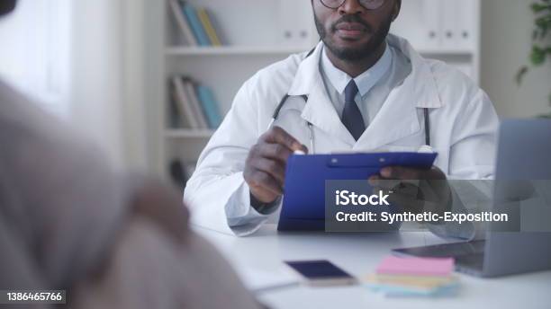 African American Gynecologist Writing Down Test Results During Pregnant Woman Health Checkup Stock Photo - Download Image Now