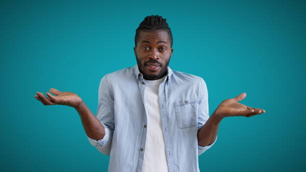 istock Young black male showing no idea gesture on blue background, feeling confused, doubt 1386468818