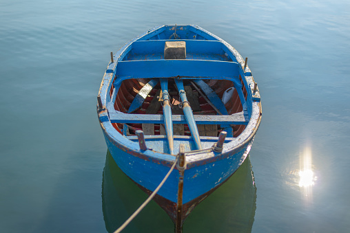 Blue Boat in lake. Sunshine on blue water. Wooden blue boat on calm water tied to the harbor by a rope.