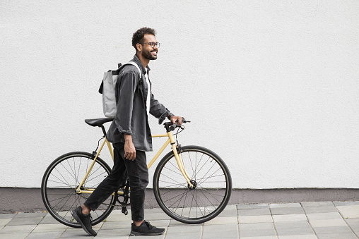 Smiling latin man riding a bike looking up outdoor. Travel, people and active lifestyle concept