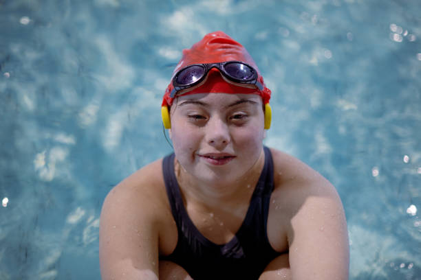 Young woman with Down syndrome swimming in swimming pool and looking at camera A young woman with Down syndrome swimming in swimming pool and looking at camera athlete with disabilities photos stock pictures, royalty-free photos & images