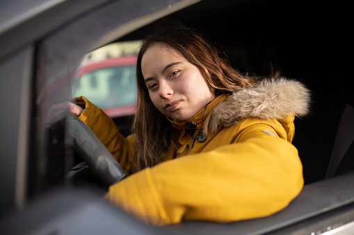 A young woman with Down syndrome driving a car and looking at camera.