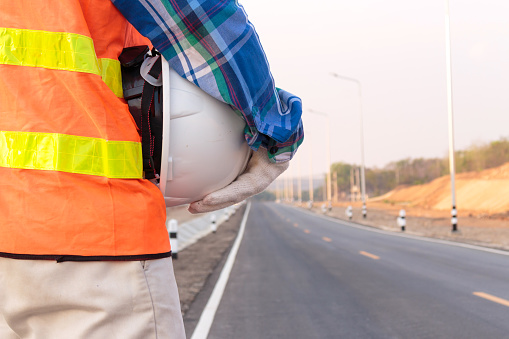 Close-up of construction worker, engineer, worker wearing life jackets and holding white safety helmets for work safety, standing on the side of the road.