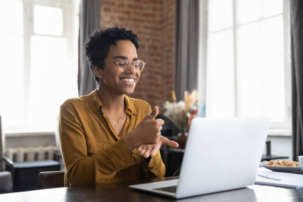 Smiling African American therapist in glasses talking on video call Smiling friendly African American therapist in glasses talking on video call, using sign language, speaking to patient with hearing disability, deafness, showing gestures at screen disability stock pictures, royalty-free photos & images