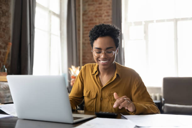 利益を数えるメガネの幸せな若いアフロアメリカの起業家の女性 - 電卓 ストックフォトと画像