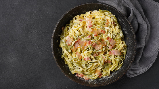 Italian egg pasta carbonara in black pan with bacon, parmesan cheese ,spices and herbs