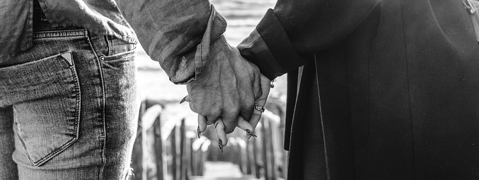 Horizontal banner with closeup of young couple holding hands walking down on wooden stair towards the beach - Hipster couple, holding hands, in love enjoying romantic evening at beach