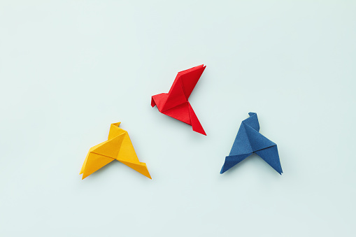three paper origami pigeons red, blue, yellow on light background