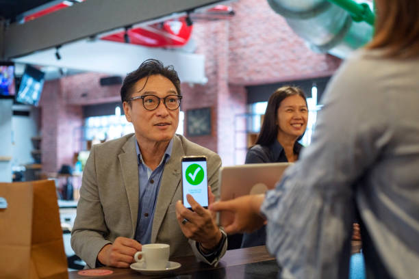 Contactless Payment in a coffee shop Smiling businessman making contactless payment using smart phone in business lounge contactless airport stock pictures, royalty-free photos & images