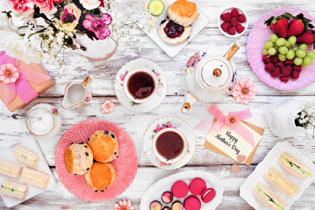 scena del tavolo da tè della festa della mamma su uno sfondo di legno bianco. biglietto di auguri, regalo, fiori, set da tè vintage, panini con le dita, cioccolatini, dessert e frutta. - afternoon tea foto e immagini stock