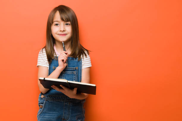 little girl writing on a notebook - child thinking writing little girls imagens e fotografias de stock