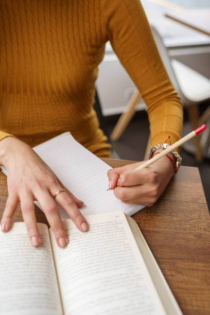 details of the hand of a person holding a pencil to make notes on a sheet of a book, intellectual work stock photo