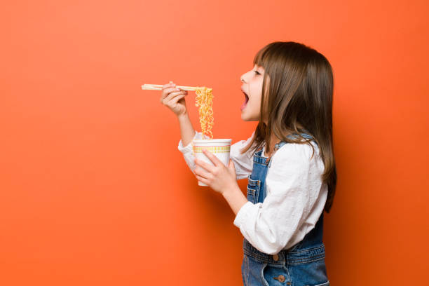 Enjoying some ramen noodles in a studio Profile view of a little girl opening a big mouth and eating noodles with chopsticks in a studio kids eating noodles stock pictures, royalty-free photos & images