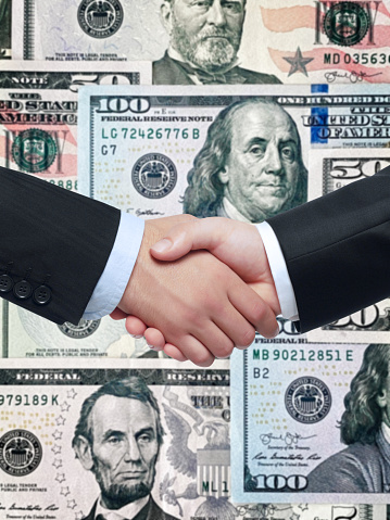 Close up shot of businessman handshaking in front of dollar bills