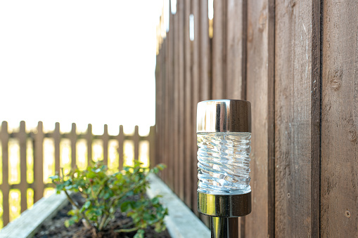 Shallow focus of garden solar light installed into a large planter in a garden. Wooden fencing is adjacent to the planter and light.