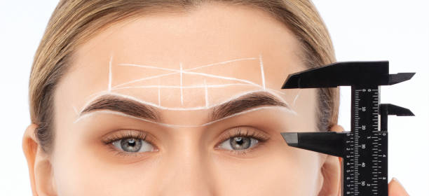 istock Make-up artist makes markings with white pencil for eyebrow and paints eyebrows. Professional makeup and facial care. 1386525446