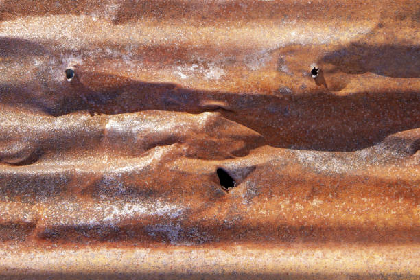 Brown abstract background with silver red hues. A weathered, rust-eaten, crumpled, perforated textured sheet of metal.