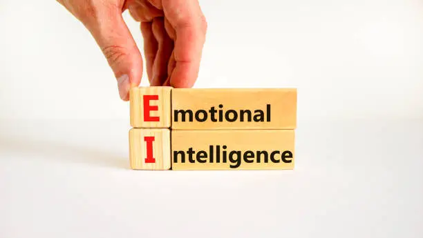 Photo of EI emotional intelligence symbol. Concept words EI emotional intelligence on wooden blocks on a beautiful white background. Psychologist hand. Business EI emotional intelligence concept, copy space.