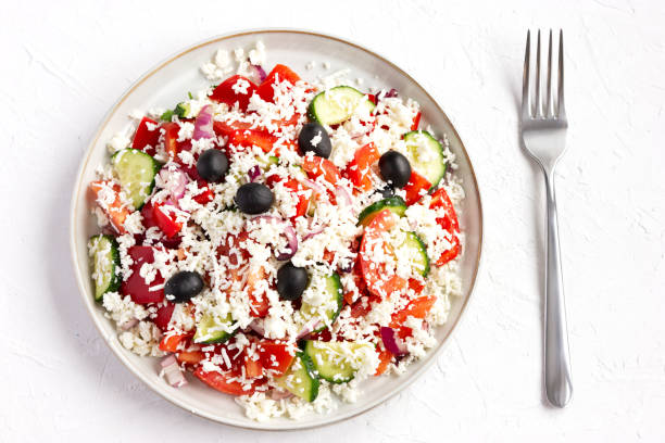 Shopska salad, is a Bulgarian cold salad popular throughout Southeastern Europe. This is Bulgaria's most famous dish and national salad. shopska salata es una ensalada sobre fondo de hormigón blanco con vista superior al tenedor. fácil de cocinar: tomates en dados, pepino, cebolla, pimiento rojo, agregue aceitunas, aceite de oliva, vinagre, perejil fresco y sal, cubra con feta